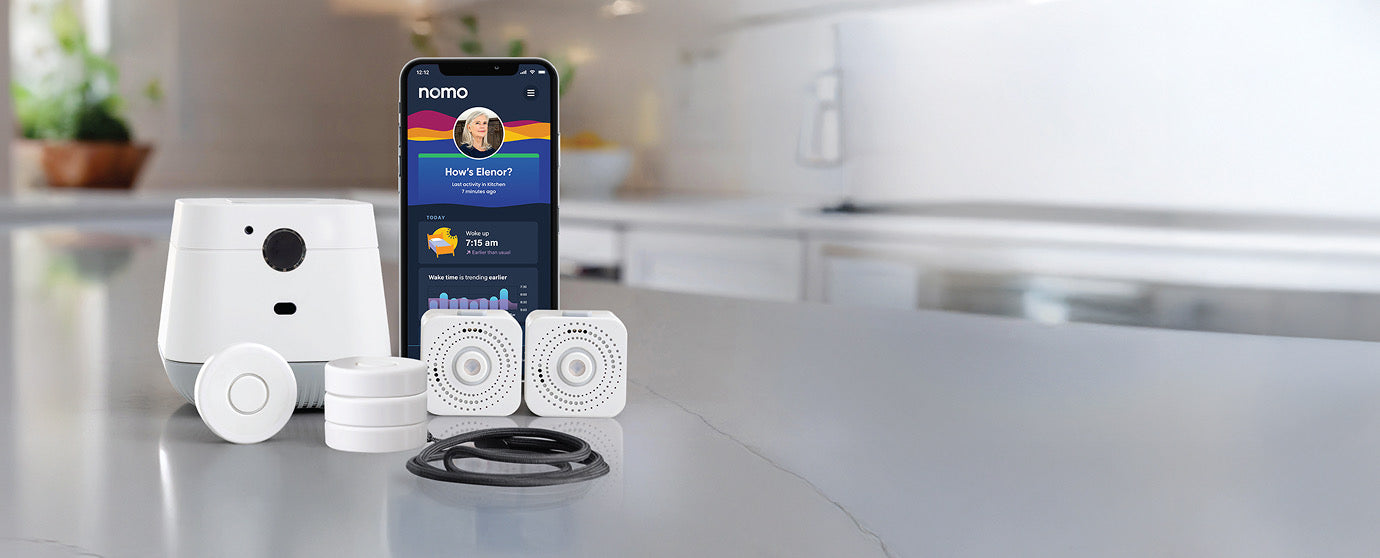 The Nomo Essential Care Kit on a kitchen counter: hub, sensors, tags, lanyard and the Nomo app showing How's Elenor?