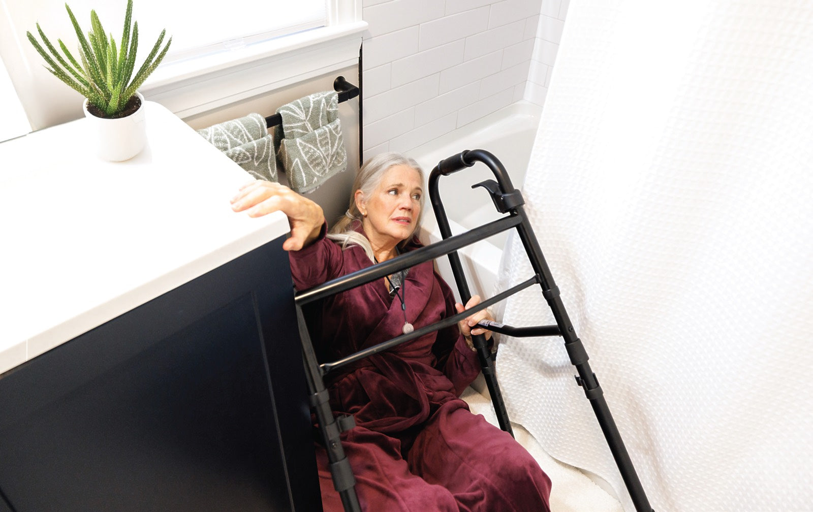 An older woman holds onto her walker after a fall beside the bathtub