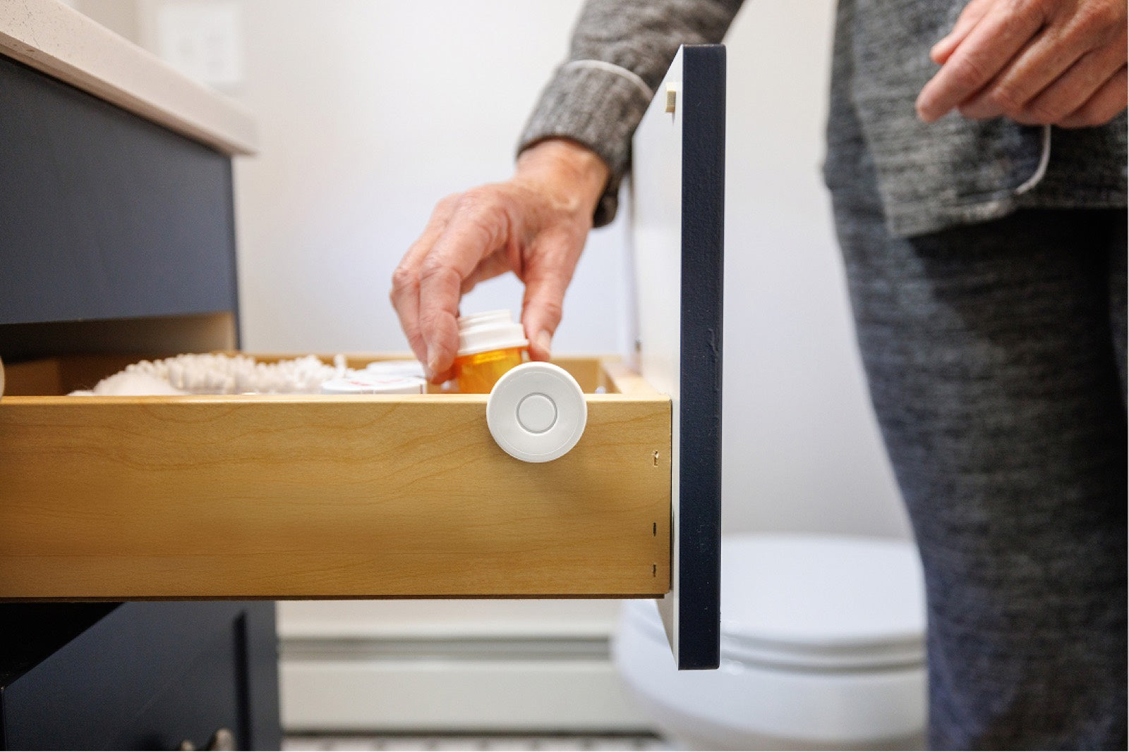 A hand reaches into a drawer of medicine bottles fitted with a Nomo Tag