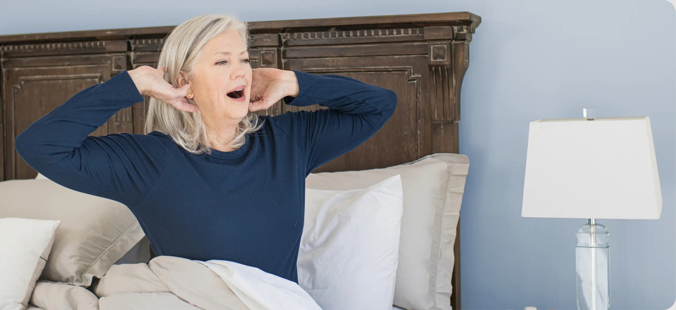 An older woman stretches as she wakes up in bed