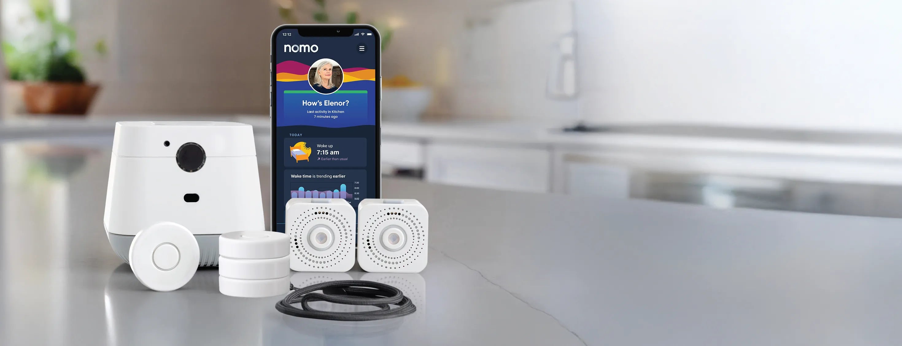 The Nomo Essential Care Kit on a kitchen counter: hub, satellites, tags, lanyard and the Nomo app
