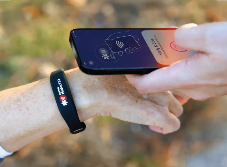 A hand holds a phone over the Nomo Medical ID bracelet on an older woman's wrist, showing Ready to Scan